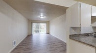 Located at 16124 SE Alder St in Portland, Oregon, this single-floor unit offers a practical and well-appointed layout designed for comfortable everyday living. The living area is bright and open, featuring light wood-style flooring throughout and a large sliding glass door fitted with vertical blinds that allows natural light to fill the room while providing access to the outdoors. The neutral-toned walls and textured ceilings contribute to a clean, understated aesthetic.

The galley-style kitchen is efficiently designed, with white cabinetry lining both sides, granite-look countertops, a tile backsplash, and a full suite of stainless steel appliances including a refrigerator and dishwasher. A utility panel is conveniently accessible near the kitchen entrance. The kitchen connects directly to the rest of the unit, creating a functional flow between spaces.

The bathroom is neatly finished with a granite-topped vanity, cream cabinetry, a wall-mounted towel bar, and tile wainscoting around the toilet area. Light wood-style flooring continues here, maintaining visual consistency throughout the unit. Additional features include wall-mounted heating units in the living space and a paneled interior door leading between rooms. The overall layout, as reflected in the dollhouse view, is compact yet well-organized, making efficient use of every square foot.