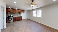 This single-floor space offers a thoughtfully designed layout that blends functionality with modern finishes throughout. The open-concept living and kitchen area is anchored by wood-look tile flooring that runs seamlessly through the space, providing warmth and durability underfoot. A ceiling fan with a light fixture keeps the living area comfortable, while a window fills the room with natural light and views of surrounding greenery.

The kitchen is a standout feature, showcasing rich, dark-stained cabinetry with ample upper and lower storage. Granite countertops provide generous prep space, complemented by a stainless steel sink and a stainless steel range. A striking mosaic tile backsplash in earthy tones of beige, brown, and gold adds texture and visual interest, tying the kitchen's design together cohesively. Recessed lighting illuminates the workspace effectively throughout.

The bathroom continues the refined aesthetic with floor-to-ceiling large-format cream-toned tiles lining the walls of the tub and shower surround. A decorative mosaic tile accent border echoes the kitchen's backsplash, creating a unified design language across the space. The combination tub and shower features chrome fixtures, completing the clean and polished look. Overall, the space presents a well-coordinated, move-in-ready interior with consistent finishes and practical design choices throughout.