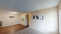 This classic single-floor unit offers a well-organized layout with one bedroom and one and a half bathrooms. The living area features a combination of wood-look hard flooring near the entryway and plush carpeting throughout the main lounge space, creating a warm and inviting atmosphere. Neutral-toned walls and a textured ceiling run throughout, providing a clean, understated backdrop. A pass-through opening connects the living area to the kitchen, enhancing the open feel between spaces.

The kitchen is equipped with white cabinetry, a double-basin sink, dark countertops, and black appliances including a refrigerator and dishwasher, all set on wood-look flooring. The bedroom is generously sized, finished with soft carpet, a ceiling fan with light fixture, and a window that allows natural light to filter in. A door leads from the bedroom to an adjoining area, offering added convenience and privacy.

The full bathroom features wood-look flooring, granite-style countertops, and a tub-shower combination. A half bath provides additional convenience for guests. Throughout the unit, central HVAC vents ensure year-round comfort. The overall ambiance is practical and comfortable, suited for straightforward, functional living.