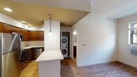 Located at 405 Broadway Street in the heart of downtown Cincinnati, Ohio, this single-floor unit offers a well-designed, functional layout with modern finishes throughout. Warm hardwood-style flooring flows seamlessly across the living, kitchen, and bedroom areas, creating a cohesive and inviting aesthetic.

The kitchen is a standout feature, showcasing rich wood cabinetry, stainless steel appliances including a full-size refrigerator and dishwasher, light-toned countertops, and a peninsula with an overhang ideal for casual dining. Pendant lighting with a distinctive warm-toned ceiling accent adds character and definition to the kitchen zone. The open layout connects the kitchen directly to the living area, which benefits from natural light through a window and a unique circular wall sconce that adds a modern design touch.

Conveniently tucked between the kitchen and bathroom is an in-unit stacked washer and dryer, offering added practicality. The bathroom features tile-surround tub and shower combination, a wood-toned vanity with light countertops, and a window that brings in natural light. The bedroom is generously proportioned with clean white walls, hardwood-style flooring, and ample room for furnishings. Throughout the unit, neutral tones, recessed lighting, and clean architectural lines contribute to a modern, comfortable living environment.