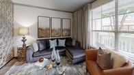 This thoughtfully designed single-floor residence offers a cohesive blend of modern finishes and warm, stylish décor across its key living spaces. The galley-style kitchen is a functional highlight, featuring dark espresso cabinetry, granite countertops, stainless steel appliances including a refrigerator, range, and microwave, pendant lighting, and wood-look flooring that extends into the adjoining areas. The open dining space connects seamlessly to the kitchen and is accented by an ornate floor mirror and decorative room divider, adding a touch of elegance to the layout. The living room is bright and inviting, with large windows that allow generous natural light, complemented by neutral wall tones and ceiling details. Two well-proportioned bedrooms each feature plush carpeting, ceiling fans, large windows with exterior views, and ample room for full bedroom suites. The primary bathroom is equipped with white shaker-style cabinetry, granite countertops, wood-look flooring, and a combination tub and shower with white tile surround. A second bathroom mirrors the same quality finishes and includes a walk-in shower. Throughout the residence, consistent use of granite surfaces, wood-look flooring, and neutral tones creates a unified and polished aesthetic.