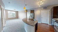 This thoughtfully designed 2-bedroom, 2-bathroom residence offers a functional and stylish layout across its single primary floor. The open-concept kitchen serves as a central focal point, featuring a curved granite-topped island with an undermount sink, dark espresso cabinetry, stainless steel appliances — including a refrigerator, range, and microwave — and striking amber pendant lighting paired with a track light fixture overhead. Hardwood flooring flows through the kitchen area, transitioning to plush carpet in the living room and bedrooms, creating a warm and comfortable ambiance throughout.

The spacious living room receives natural light through large windows fitted with blinds. A glass-panel door leads to a private balcony with exterior views of surrounding greenery. The generously sized primary bedroom includes direct access to an en-suite bathroom equipped with a walk-in glass-door shower featuring white tile surround. The second bathroom offers a full soaking tub with a tiled surround. Both bathrooms are finished with dark vanity cabinetry. The second bedroom is well-proportioned and bright. The residence also includes a hallway, closet, and neutral warm-toned walls throughout, contributing to a clean, move-in-ready aesthetic.