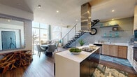 This sophisticated two-story residence offers a seamless blend of modern design and functional living across two generously sized floors. The main level features an open-concept layout where the kitchen, dining, and living areas flow effortlessly together. The kitchen is well-appointed with warm wood cabinetry, stainless steel appliances, a gas cooktop island with a statement stainless steel range hood, and clean white countertops. The adjacent dining area provides an intimate setting, while the living room commands attention with dramatic double-height ceilings, floor-to-ceiling windows, and sweeping panoramic views that flood the space with natural light. A sleek open-tread staircase with glass railings leads to the upper level, which includes a versatile open loft area, the bedrooms, and additional living space. The expansive primary bedroom features sliding glass doors to a private balcony with scenic views. The spa-inspired primary bathroom offers large-format tile, a walk-in open shower, a soaking tub, and built-in niche shelving. A dedicated laundry room with side-by-side washer and dryer adds everyday convenience. Rich hardwood-style flooring, teal accents, and curated artwork complete this home's refined, contemporary aesthetic.