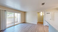Located at 3825 Little Rock Drive in Antelope, California, this single-story, one-bedroom, one-bathroom home offers a practical and well-organized layout. The combined kitchen and living room serves as the heart of the space, featuring light wood-look flooring, warm neutral-toned walls, and a ceiling fan with integrated lighting. The kitchen is equipped with white cabinetry, ample counter space, a double-basin sink, a white electric range, and a full-size refrigerator — all laid out in an efficient galley-style configuration. The living area benefits from a large sliding glass door that opens to a private balcony, filling the room with natural light and providing outdoor views of surrounding trees. The bedroom is a comfortable, well-proportioned room finished with soft carpeting and vertical blinds over a window that overlooks greenery. A dedicated closet provides convenient storage. The bathroom features a full tub-shower combo with clean white surround, wood-look flooring, and safety grab bars. A hallway connects the rooms, contributing to the home's efficient flow. Throughout, the consistent warm beige palette and clean finishes create a simple, welcoming ambiance.