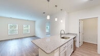 Located at 7112 Mechanicsville Turnpike in Mechanicsville, Virginia, this single-floor, 3-bedroom, 2-bathroom residence offers a clean, modern aesthetic with thoughtfully designed living spaces. The open-concept kitchen and living area serves as the heart of the home, featuring a central island with granite-style countertops, white shaker cabinetry, stainless steel appliances—including a refrigerator, range, microwave, and dishwasher—and stylish pendant lighting overhead. Light wood-style flooring flows throughout the main living areas, complementing the bright, neutral color palette. Two windows in the living area allow natural light to fill the space, creating an airy, welcoming atmosphere.

The primary bedroom is a comfortable, well-proportioned room with plush carpeting and a window providing natural light. Its en-suite bathroom features a dual-sink vanity with granite-style countertops, white cabinetry, and wood-style flooring. The two additional bedrooms also feature carpet and windows with exterior views. A second full bathroom includes a tub/shower combination with brushed nickel fixtures. The unit also includes a dedicated utility room and closet for added storage and functionality.