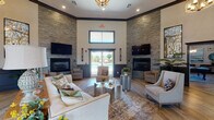 Located on Bridgewater Drive in Clarksville, Tennessee, this single-story community clubhouse offers a thoughtfully designed collection of amenity spaces built for both relaxation and entertainment. The centerpiece of the facility is a spacious lounge area defined by soaring ceilings, light hardwood flooring, and dramatic stacked-stone accent walls that flank two linear fireplaces. Mounted flat-screen televisions accompany each fireplace, while large glass doors at the rear provide direct views of the outdoor pool area, drawing in natural light and creating a seamless indoor-outdoor connection.

Adjacent to the lounge is a well-appointed kitchen featuring rich warm-toned cabinetry, granite countertops, a white stacked-tile backsplash, and a stone-clad island with bar seating and pendant lighting overhead. Stainless steel appliances and ample cabinet storage make the space highly functional for gatherings.

A dedicated theater room provides a cinematic experience with tiered stadium-style seating, plush reclining chairs, wall sconces, dark paneled wainscoting, and a large projection screen. A separate billiards room, visible through a wide doorway from the lounge, offers additional recreational space. Together, these areas create a versatile and polished community hub.