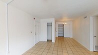 This single-floor, 2-bedroom, 2-bathroom residence offers a practical and well-organized layout designed for comfortable living. The entry opens into a bright foyer area with light tile flooring, a coat closet, and built-in shelving — ideal for storage and display. The living room is generously sized, featuring the same tile flooring, a ceiling fan with light fixture, and a sliding glass door that allows natural light to fill the space. A dedicated dining area adjoins the living space and includes a chandelier and additional built-in shelving. The galley-style kitchen is efficiently designed with white cabinetry, tile countertops, a double sink, electric range, and a full-size refrigerator, providing ample storage and prep space. Both bedrooms are carpeted and offer a comfortable, quiet retreat, each equipped with a closet featuring a full-length hanging rod. The bedrooms are served by two full bathrooms, each featuring a single-sink vanity with wood cabinetry, tile flooring, a large wall mirror, and a tub-shower combination with an arched surround. The overall design is clean and neutral, offering a versatile canvas throughout.
