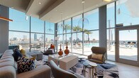 This contemporary amenity floor is defined by its bold design aesthetic, soaring floor-to-ceiling glass walls, and an energetic use of color throughout. The expansive resident lounge anchors the space, featuring high ceilings, dramatic pendant lighting, and a wall of curtain-glass windows that frame panoramic views of the outdoor pool deck, palm trees, and the city skyline beyond. Thoughtfully curated seating arrangements — including sculptural lounge chairs, modular sofas, and patterned area rugs — create distinct zones for relaxation and socializing.

Adjacent to the lounge, a well-appointed social kitchen and dining area showcases a striking vertically-striped accent wall in warm tones, built-in appliances, white communal tables, and dual flat-screen displays, making it ideal for both casual gatherings and shared meals. A dedicated games and entertainment zone provides a foosball table, casual seating clusters, and additional large windows fitted with decorative lattice screens that diffuse natural light beautifully.

The corridors feature vibrant teal walls, large-format tile flooring, and elevator access, connecting the amenity spaces with ease. Throughout, the design balances vivid accent colors — orange, green, teal, and yellow — with clean architectural lines to create a dynamic yet welcoming communal environment.