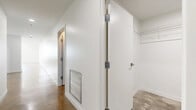 This well-appointed one-bedroom, two-bathroom unit offers a modern, urban aesthetic across a generous single floor. Polished concrete floors flow throughout the entire space, lending an industrial-chic character that ties each room together seamlessly. The open-concept living and kitchen area is bright and airy, anchored by large floor-to-ceiling windows that frame impressive city skyline views and flood the space with natural light. The kitchen features a peninsula-style counter, white cabinetry, and stainless steel appliances, including a built-in microwave. The spacious primary bedroom offers high ceilings with exposed ductwork, adding to the loft-like feel, and connects to a dedicated hallway leading to the private rooms. Both bathrooms are finished in clean white tile, with one featuring a standalone walk-in shower and a soaking tub alongside a gray vanity with a white countertop, and the other offering a deep soaking tub with mosaic tile surround. A generously sized walk-in closet provides ample storage with wire shelving and hanging rods. A dedicated laundry room houses a full-size washer and dryer, completing the practical amenities of this thoughtfully designed urban residence.