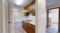Located at 1250 Autumn Dr in Faribault, MN, this one-bedroom, one-bathroom unit offers a well-organized single-floor layout designed for functional, comfortable living. The galley-style kitchen is a standout feature, outfitted with warm oak cabinetry spanning both upper and lower sections, a double-basin stainless steel sink with marble-patterned countertops, a white electric range with overhead ventilation, and a full-size refrigerator. Light hardwood-style vinyl flooring runs throughout the kitchen and connects seamlessly to the adjoining dining and living areas, both of which benefit from natural light streaming through window blinds and baseboard heating for year-round comfort. The bedroom is finished with plush carpeting, a wood-framed window with exterior views, and access to generous closet storage — three closets are distributed throughout the unit, offering practical organization solutions. The bathroom features tile flooring, a wood-toned vanity with a white countertop, and clean, neutral finishes. Neutral wall tones and warm wood trim carry throughout the entire space, creating a cohesive and inviting atmosphere. The layout flows efficiently from the entry hallway through each room, making the most of the available footprint.