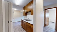 Located at 1250 Autumn Dr in Faribault, MN, this one-bedroom, one-bathroom unit offers a well-organized single-floor layout designed for functional, comfortable living. The galley-style kitchen is a standout feature, outfitted with warm oak cabinetry spanning both upper and lower sections, a double-basin stainless steel sink with marble-patterned countertops, a white electric range with overhead ventilation, and a full-size refrigerator. Light hardwood-style vinyl flooring runs throughout the kitchen and connects seamlessly to the adjoining dining and living areas, both of which benefit from natural light streaming through window blinds and baseboard heating for year-round comfort. The bedroom is finished with plush carpeting, a wood-framed window with exterior views, and access to generous closet storage — three closets are distributed throughout the unit, offering practical organization solutions. The bathroom features tile flooring, a wood-toned vanity with a white countertop, and clean, neutral finishes. Neutral wall tones and warm wood trim carry throughout the entire space, creating a cohesive and inviting atmosphere. The layout flows efficiently from the entry hallway through each room, making the most of the available footprint.