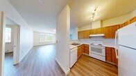 Located in Seattle's Broadview neighborhood, this two-bedroom, two-bathroom apartment offers a thoughtfully designed single-floor layout. Light vinyl plank flooring runs throughout, providing a clean, cohesive look across every room. The open living area is bright and airy, anchored by a large picture window that fills the space with natural light and offers views of the surrounding greenery. The kitchen is well-equipped with warm honey-toned cabinetry, white appliances including a range, dishwasher, and refrigerator, plus ample counter space and a functional U-shaped layout. A pass-through area connects the kitchen to the living space, enhancing the open feel. The generously sized primary bedroom features a sliding double-door closet, while a separate walk-in closet provides additional storage. Both bathrooms are finished with warm wood-toned vanities, white countertops, and large mirrors. One bathroom includes a sliding glass shower enclosure. A hallway connects the bedrooms and bathrooms, keeping the layout practical and private. Throughout the unit, clean white walls, simple trim, and consistent flooring create a calm, neutral atmosphere ready for personalization.