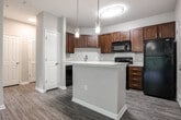 Located at 5462 Whittlesey Blvd in Columbus, Georgia, this single-floor residence offers a thoughtfully designed open-concept layout. The kitchen is equipped with rich dark wood cabinetry, stainless steel appliances including a range and over-the-range microwave, and a peninsula with bar seating that flows seamlessly into the dining and living areas. Decorative pendant lighting and wood-look flooring throughout the main living spaces add warmth and style. The living room features crown molding, a ceiling fan, and French doors that invite natural light and outdoor views. A decorative column elegantly defines the transition between spaces. The primary bedroom is carpeted, bathed in natural light from large windows, and connects to a private en-suite bathroom with a glass-enclosed shower, dark wood vanity, and tile flooring. A second bedroom, also carpeted with generous natural light, is served by a full hallway bathroom featuring a soaking tub with tiled surround and a wood-vanity with ample counter space. A dedicated in-unit laundry room with a full-size washer and dryer and built-in shelving adds everyday convenience. The overall ambiance is clean, modern, and functional.