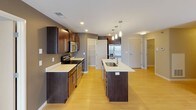 This single-floor residence offers a thoughtfully designed layout with modern finishes and functional living spaces. The kitchen serves as the centerpiece of the home, showcasing rich dark wood cabinetry, light quartz countertops, and a full suite of stainless steel appliances including a range, microwave, and refrigerator. A large central island with an integrated sink provides additional prep space and casual seating, while pendant lighting adds a contemporary touch overhead. Light wood-style flooring runs throughout the main living and kitchen areas, complementing the warm, neutral color palette. A dedicated pantry with built-in shelving offers convenient additional storage directly off the kitchen. The bedrooms feature plush carpet flooring, neutral walls, and windows with blinds that allow for natural light. Each bedroom is supported by well-organized closet space equipped with wire shelving systems for efficient storage. The bathroom includes a dark wood vanity with a light countertop, a mirror with overhead lighting, and a full tub-shower combination. A dedicated laundry area houses a side-by-side top-load washer and dryer, complete with an overhead wire shelf for added utility. The overall design is clean, modern, and practical, creating a comfortable and cohesive living environment.
