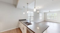 Located at 134 Village Club Dr in Mooresville, NC, this well-appointed single-floor home offers three bedrooms and three full bathrooms within a thoughtfully designed layout. The open-concept living and dining area is finished with light hardwood-style flooring, crown molding, and an abundance of natural light streaming through multiple windows with blinds. A ceiling fan and elegant chandelier add to the space's refined yet functional character.

The kitchen serves as a central hub, featuring a spacious quartz island with a double stainless steel undermount sink, white cabinetry with brushed nickel hardware, and pendant lighting overhead. The kitchen flows seamlessly into the dining and living areas, making it ideal for entertaining.

All three bedrooms are carpeted for comfort, each equipped with ceiling fans and natural light from windows. The primary bedroom includes a private en-suite bathroom with dark granite countertops, a single vanity, white cabinetry, and a glass-enclosed shower. A secondary bathroom features marble-look tiled tub/shower surround and hardwood-style flooring.

A dedicated laundry room houses a full-size washer and dryer with overhead shelving. Two closets and a hallway round out the functional layout, making this home as practical as it is inviting.