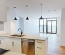 This contemporary apartment at 100 Fullarton Street, London ON, offers 740 square feet of efficiently designed living space. The unit features two bedrooms, including a primary bedroom of 180 square feet, and two full bathrooms. The open-concept layout seamlessly integrates the kitchen and living areas, creating a spacious feel within the compact footprint.

The kitchen is a highlight, boasting modern white cabinetry, stainless steel appliances, and a stylish tile backsplash. Pendant lighting and a central island with a sink enhance both functionality and aesthetic appeal. Throughout the apartment, light hardwood flooring adds warmth and continuity.

Large floor-to-ceiling windows in the living area and bedrooms flood the space with natural light and provide stunning panoramic views of the city. The bathrooms are sleek and modern, featuring clean lines, floating vanities, and glass-enclosed showers.

The apartment's design maximizes space utilization with built-in closets and storage solutions. Recessed lighting and contemporary fixtures contribute to the overall modern ambiance. This well-appointed unit offers a perfect blend of style and practicality in an urban setting.