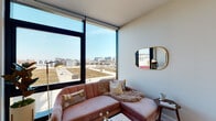 This single-floor residence showcases a sleek, contemporary design characterized by expansive floor-to-ceiling windows that frame sweeping urban skyline views, flooding the interior with abundant natural light. The open layout connects the primary living areas seamlessly, creating a cohesive flow throughout the space.

The living area is anchored by large corner windows with roller shades, offering panoramic city views and a bright, airy atmosphere. Light hardwood flooring runs throughout, complementing the clean white walls and modern aesthetic.

The bedroom continues the floor-to-ceiling window design, providing unobstructed cityscape views and ample natural light. The space is well-proportioned, with light wood floors and crisp white walls contributing to a calm, restful environment.

The kitchen features a refined, modern design with two-tone cabinetry—warm wood lower cabinets paired with light upper cabinets—complemented by white quartz countertops and a marble-look tile backsplash. Stainless steel appliances, including a gas range, dishwasher, refrigerator, and over-range microwave, complete the functional and stylish space.

The bathroom offers a clean, minimalist aesthetic with a floating wood-tone vanity, white quartz countertop, undermount sink, and a large wall mirror, reinforcing the modern sensibility found throughout the residence.