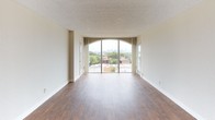 This 2-bedroom, 2-bathroom unit is designed with a practical, single-story layout that makes efficient use of its space. The living area serves as the centerpiece of the unit, featuring rich wood-style flooring and a striking floor-to-ceiling arched sliding glass door that opens to a balcony with expansive city skyline views, flooding the room with natural light.

The galley-style kitchen is positioned adjacent to the living area and features wood-toned cabinetry extending to the ceiling, a double stainless steel sink, a coil-burner range, a refrigerator, and a dishwasher. Overhead lighting and ample counter space make the kitchen both functional and practical.

Both bedrooms are carpeted and well-proportioned, each offering large sliding-door closets that provide generous storage capacity. One bedroom also features access to an additional closet, further enhancing storage options. Large sliding glass doors in the bedrooms bring in natural light and offer elevated outdoor views.

The two bathrooms differ in configuration. The primary bathroom includes a full-width vanity mirror with globe lighting, a single sink, a tiled shower-tub combination, and wood-style flooring. The second bathroom features a narrower layout with a countertop vanity, toilet, and tub, also finished with wood-style flooring. Both bathrooms maintain a clean, neutral aesthetic consistent with the rest of the unit.