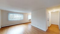 Located at Bay Shore Gardens in Bay Shore, NY, this single-floor residence offers a clean, functional layout designed for comfortable everyday living. The spacious main living area immediately draws attention with its warm hardwood flooring, crisp white walls, and generous natural light streaming through multiple windows dressed with vertical blinds. Baseboard heating and wall-unit air conditioning ensure year-round climate control throughout the space.

A dedicated hallway connects the living area to the private rooms, featuring rich hardwood flooring and a light blue accent wall that adds a subtle touch of character. The hallway also includes a paneled door providing convenient access to additional storage or closet space.

The bedroom continues the home's consistent aesthetic, with hardwood flooring, a window with a vertical blind treatment, baseboard heating, and a wall-unit air conditioner, creating a comfortable and well-ventilated retreat.

The kitchen is well-appointed with white cabinetry, stone-patterned countertops, tile flooring, stainless steel appliances including a refrigerator and gas range, and a window overlooking the outdoors, filling the space with natural light.

The bathroom is finished with classic white subway tile surrounding a full soaking tub and shower combination, complemented by a natural light source from a window above.