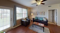 Located at Jefferson Commons in Kalamazoo, Michigan, this single-floor residence offers a well-organized layout designed for comfortable everyday living. The living room is a welcoming central space featuring rich hardwood-style flooring, large windows that invite natural light and outdoor views, and a ceiling fan overhead. The kitchen is efficiently designed with ample cabinetry in a neutral finish, dark granite-style countertops, white appliances including a range and built-in microwave, and matching hardwood-style flooring that ties the common areas together. The full bathroom continues the cohesive aesthetic with a tub-shower combination, a vanity with granite-style countertops, built-in overhead cabinetry, and hardwood-style flooring. Multiple bedrooms are carpeted for comfort and each features windows with blinds and curtains for natural light and privacy. Several bedrooms include built-in desks and mirrored sliding-door closets, making them well-suited for both rest and study. The neutral wall tones throughout the residence create a clean, versatile backdrop. Overall, the space is practical and functional, offering a comfortable living environment conveniently situated near Western Michigan University.