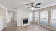 Located at 9939 Quail Blvd in Austin, TX, this two-bedroom, one-bathroom single-floor home offers a well-organized layout with a neutral color palette and a mix of wood-look flooring and plush carpet throughout. The open living room serves as the heart of the home, highlighted by a tile-surround fireplace, a ceiling fan with light fixture, and a bank of windows fitted with blinds that allow ample natural light to fill the space. Built-in shelving niches along one wall provide display and storage options. The kitchen runs along a galley-style corridor with white cabinetry, wood-look flooring, and black appliances including a refrigerator and range. A pass-through counter connects the kitchen to the living area, enhancing the open feel. Both bedrooms feature soft carpeting, textured ceilings, and windows with blinds. The primary bedroom is generously sized and offers direct access to the shared bathroom. A hallway connects the bedrooms to the full bathroom, which features clean white finishes and a tub-shower combination. Two closets provide additional storage throughout. Textured ceilings are consistent across all rooms, lending a classic residential character to this Austin home.