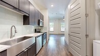 Located at 3964 Watercourse Dr in Fort Worth, TX, this efficiently designed single-floor unit offers a thoughtful layout comprising a living room, kitchen, bathroom, and closet. Dark-toned hardwood-style flooring runs continuously throughout, providing a warm contrast against crisp white walls and trim.

The kitchen is a standout feature, appointed with dark espresso cabinetry, light quartz countertops, and a full suite of stainless steel appliances including a range, microwave, dishwasher, and refrigerator. A soft green subway tile backsplash adds a subtle accent, while an undermount sink with a modern faucet completes the functional workspace.

The living area is bright and open, benefiting from multiple windows that invite natural light and offer views of surrounding greenery. Ceiling height adds a sense of openness to the space, and a ceiling fan provides practical comfort.

The bathroom is well-appointed with a tub-shower combination featuring white subway tile surround, wood-look flooring, and dark vanity cabinetry consistent with the kitchen's design language.

The walk-in closet provides organized storage with dual hanging rods and shelving on two walls. A distinctive paneled white interior door design is carried throughout the unit, lending a cohesive, modern aesthetic from entry to every room.