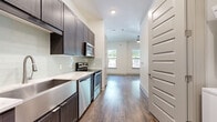 Located at 3964 Watercourse Dr in Fort Worth, TX, this efficiently designed single-floor unit offers a thoughtful layout comprising a living room, kitchen, bathroom, and closet. Dark-toned hardwood-style flooring runs continuously throughout, providing a warm contrast against crisp white walls and trim.

The kitchen is a standout feature, appointed with dark espresso cabinetry, light quartz countertops, and a full suite of stainless steel appliances including a range, microwave, dishwasher, and refrigerator. A soft green subway tile backsplash adds a subtle accent, while an undermount sink with a modern faucet completes the functional workspace.

The living area is bright and open, benefiting from multiple windows that invite natural light and offer views of surrounding greenery. Ceiling height adds a sense of openness to the space, and a ceiling fan provides practical comfort.

The bathroom is well-appointed with a tub-shower combination featuring white subway tile surround, wood-look flooring, and dark vanity cabinetry consistent with the kitchen's design language.

The walk-in closet provides organized storage with dual hanging rods and shelving on two walls. A distinctive paneled white interior door design is carried throughout the unit, lending a cohesive, modern aesthetic from entry to every room.