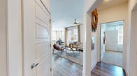 This thoughtfully designed single-floor residence offers a seamless blend of modern finishes and warm, inviting aesthetics. The entryway, accented by a decorative sunburst mirror, opens into a spacious living area featuring rich hardwood-style flooring, a ceiling fan, and generous natural light streaming through large windows dressed with linen drape panels and horizontal blinds. A rustic wood console table and leather accent chairs lend character to the living space.

The dining area is bathed in natural light from a wraparound arrangement of windows with outdoor views, creating a bright and airy atmosphere ideal for gathering. The kitchen is a standout, boasting white shaker cabinetry, granite countertops, a large island with bar seating, subway tile backsplash, and stainless steel appliances — all finished with recessed lighting overhead.

The primary bedroom features a ceiling fan, soft carpeting, and a soothing sage-green accent wall, providing a calm and restful retreat. A secondary bedroom with carpet, natural light, and a pendant light fixture offers flexible use. The bathroom includes white cabinetry, granite countertops, a large vanity mirror, and hardwood-style flooring, combining functionality with clean, modern design throughout.