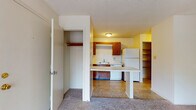 Located at 2509 Avent Ferry Rd in Raleigh, NC, this single-floor unit offers a practical and comfortable layout designed for everyday living. The kitchen is equipped with warm wood cabinetry, white appliances including a coil-top electric range, refrigerator, and dishwasher, complemented by light countertops and a stainless steel sink. A built-in breakfast bar extends into the adjoining living area, creating a natural transition between the two spaces. The living area features neutral carpet flooring and leads directly to a sliding glass door that opens onto a private balcony, offering pleasant outdoor views of the surrounding neighborhood and trees. A wall-mounted HVAC unit provides climate control in the main living space. The bedroom is carpeted and bright, with a window framing lush tree views and providing ample natural light. Ample storage is available throughout, including a dedicated closet and open shelving. The bathroom features a full-size soaking tub with a clean, molded surround and chrome fixtures. Textured ceilings are consistent throughout the unit, and the overall color palette of warm yellows, whites, and neutral tones lends the space a cozy, welcoming ambiance.