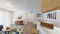 This single-floor unit showcases a thoughtfully arranged layout with distinct living, dining, and sleeping areas. The living room is an inviting space anchored by wood-look hard flooring, a large sliding glass door that draws in natural light and provides outdoor views, and a textured ceiling throughout. A half-wall peninsula seamlessly connects the living area to the galley-style kitchen, which features white cabinetry with wood trim accents, white appliances, ample upper and lower cabinet storage, and a double-basin sink with generous counter space on either side.

Adjacent to the living room, a dedicated dining area provides space for a full table setup, making it well-suited for everyday meals or entertaining. The bedroom is carpeted for comfort and includes a notably large window that allows abundant natural light, along with access to a spacious walk-in closet with built-in shelving and hanging rods. The bathroom features an extended vanity countertop with a wide mirror and lighted medicine cabinet, paired with wood-look flooring that carries through from the main living areas. Throughout the unit, a neutral color palette and consistent design details create a cohesive and functional living environment.