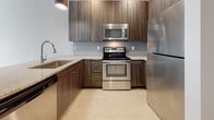 This single-story unit offers a well-designed open-concept layout with modern finishes throughout. The living and dining area features light wood-look tile flooring and a large window that fills the space with natural light, providing views of the surrounding building exterior. The seamlessly connected kitchen is outfitted with dark wood cabinetry, granite countertops, a subway tile backsplash, and a full suite of stainless steel appliances, including a refrigerator, range, and built-in microwave. A peninsula with a matching gray cabinet base adds additional prep and seating space.

The bedroom is carpeted for comfort and includes a ceiling fan, a window for natural light, and access to a spacious walk-in closet equipped with wire shelving and hanging rods along multiple walls, offering generous storage capacity.

The full bathroom features wood-toned cabinetry with a granite countertop vanity, a large mirror, and light wood-look tile flooring. A full tub and shower combo with white subway tile surround and a rainfall-style showerhead completes the space. The overall aesthetic is clean, contemporary, and cohesive throughout.
