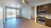 This thoughtfully designed single-floor residence offers a clean, contemporary aesthetic throughout. The open-concept living area is anchored by light hardwood-style flooring and track lighting, creating a bright and welcoming atmosphere. Sliding glass doors lead to a balcony, filling the space with natural light and providing views of the surrounding area.

The kitchen is a standout feature, showcasing flat-front wood-toned cabinetry, light countertops, a white subway tile backsplash, and a full suite of stainless steel appliances including a side-by-side refrigerator with ice maker, dishwasher, range, and built-in microwave. A stainless steel sink completes the functional layout.

The bedrooms are finished with plush carpeting and feature windows fitted with horizontal blinds, allowing for natural light and outdoor views. The bathroom is clean and modern, offering a full soaking tub and shower combination surrounded by classic white subway tile, complemented by a wood-toned vanity with light countertops.

A dedicated in-unit laundry closet houses a stacked washer and dryer, adding everyday convenience. Throughout the space, neutral tones, consistent finishes, and efficient layouts combine to deliver a comfortable and practical living environment.