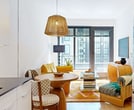 This 410 square foot apartment in Washington, DC offers a thoughtful balance of functionality and style within a compact space. The single-floor layout comprises a bedroom, bathroom, living room, and kitchen, expertly designed to maximize every inch.

The bedroom, measuring 90 square feet, features a queen-sized bed with a rattan headboard and is adorned with a striking fan-shaped wall art piece. Floor-to-ceiling windows flood the room with natural light and offer urban views, while blackout blinds ensure privacy.

The living area showcases a vibrant yellow sofa, adding a pop of color to the neutral palette. A glass coffee table and stylish floor lamp complete the space, creating a cozy yet modern atmosphere. The open-plan design seamlessly connects to the kitchen, which boasts sleek white cabinetry, stainless steel appliances, and ample counter space.

The bathroom presents a contemporary design with contrasting black and white tiles, a glass-enclosed shower, and a floating vanity. Wood accents provide warmth to the otherwise monochromatic scheme.

Throughout the apartment, warm wood flooring unifies the space, while strategic lighting enhances the ambiance. Despite its modest size, the clever layout and thoughtful design elements create a surprisingly spacious feel in this urban dwelling.