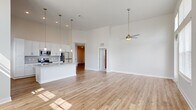 Located on City View Loop in Midlothian, VA, this two-bedroom, two-bathroom single-floor residence offers a well-designed open layout with impressive architectural details throughout. The combined kitchen and living area is the heart of the home, anchored by dramatically tall ceilings that lend an expansive, airy feel. A ceiling fan adds both style and function to the living space, which is bathed in natural light streaming through large windows with city and tree views. The kitchen is outfitted with crisp white shaker cabinetry, granite countertops, a central island with a sink, stainless steel appliances, and elegant pendant lighting — a cohesive and functional design. Light-toned hardwood-style flooring runs throughout the main living areas, while plush carpet adds warmth to both bedrooms. The primary bedroom is generously proportioned, featuring soaring ceilings, a ceiling fan, large windows, and direct access to a walk-in closet with built-in wire shelving. Both bathrooms echo the home's refined palette, showcasing white cabinetry, granite vanity tops, and hardwood-style flooring. A clean, bright hallway connects the private quarters to the living areas, completing a thoughtful and cohesive floor plan.