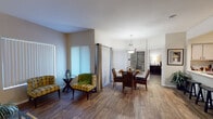 This thoughtfully designed single-floor residence offers a seamless blend of comfort and functionality across its well-defined living spaces. Rich hardwood-style flooring flows throughout, tying each room together with a warm and cohesive aesthetic.

The open living room is a standout, featuring elevated ceilings, a built-in arched niche ideal for display, and large windows with vertical blinds that invite abundant natural light. A dedicated dining area sits adjacent, centered beneath a statement pendant light fixture and surrounded by generous window coverage.

The kitchen features a pass-through bar with counter seating, ample cabinetry, stainless steel appliances, and track lighting overhead — creating a practical yet stylish space that connects easily to the main living areas.

Both bedrooms are comfortably sized, each with ceiling fans, hardwood-style flooring, and large windows. The primary bedroom includes access to a walk-in closet, providing excellent storage. The bathrooms are well-appointed with wide vanities, large mirrors, and clean, neutral finishes.

A dedicated in-unit laundry area houses a full-size washer and dryer with additional shelving for storage. Throughout the residence, neutral wall tones, consistent flooring, and considered lighting create a calm, welcoming ambiance.