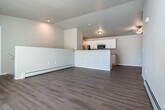 This two-story space offers a practical and comfortable layout spread across two levels, connected by a carpeted staircase with a white handrail set against textured walls. The kitchen is designed with a galley-style layout, featuring white shaker cabinetry, granite-look countertops, a stainless steel sink, and stainless steel appliances including a refrigerator and range. Light wood-look flooring runs throughout the main living areas, complementing the bright, neutral color palette. An open living area benefits from a baseboard heating system and vaulted ceiling detail, adding an airy quality to the space. The bedrooms are finished with plush carpet and include sliding-door closets with wire shelving for organized storage. Ceiling fans with integrated lighting fixtures provide both comfort and illumination. The bathrooms are cleanly appointed, with one featuring a walk-in shower with built-in shelving and chrome fixtures, and another offering a full tub-shower combination alongside a white vanity with granite-look countertops and cabinetry above the toilet. A dedicated laundry room includes a full-size washer and dryer, wood-look flooring, and built-in wire shelving for additional storage. The attached garage provides secure parking and features an automatic door opener, offering convenient access and extra utility space.
