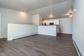 This two-story space offers a practical and comfortable layout spread across two levels, connected by a carpeted staircase with a white handrail set against textured walls. The kitchen is designed with a galley-style layout, featuring white shaker cabinetry, granite-look countertops, a stainless steel sink, and stainless steel appliances including a refrigerator and range. Light wood-look flooring runs throughout the main living areas, complementing the bright, neutral color palette. An open living area benefits from a baseboard heating system and vaulted ceiling detail, adding an airy quality to the space. The bedrooms are finished with plush carpet and include sliding-door closets with wire shelving for organized storage. Ceiling fans with integrated lighting fixtures provide both comfort and illumination. The bathrooms are cleanly appointed, with one featuring a walk-in shower with built-in shelving and chrome fixtures, and another offering a full tub-shower combination alongside a white vanity with granite-look countertops and cabinetry above the toilet. A dedicated laundry room includes a full-size washer and dryer, wood-look flooring, and built-in wire shelving for additional storage. The attached garage provides secure parking and features an automatic door opener, offering convenient access and extra utility space.