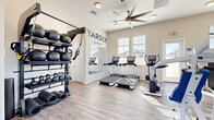 The Yardly McDowell fitness center at 9200 W McDowell Rd in Phoenix, AZ is a thoughtfully designed, single-floor community gym that offers a comprehensive range of exercise equipment in a bright, modern setting. The space features light wood-style flooring and neutral walls, creating a clean and welcoming atmosphere throughout.

The cardio zone is equipped with multiple treadmills, an elliptical, a stationary bike, and a rowing machine, all positioned to take advantage of the abundant natural light streaming through large, white-shuttered windows. Ceiling fans overhead ensure comfortable airflow during workouts.

A dedicated strength training area houses a multi-station cable machine, a rack with weight plates, adjustable benches, and an extensive dumbbell rack offering a wide range of weights. This section is complemented by a full-length wall mirror, allowing users to monitor their form effectively.

A functional training station features a wall-mounted TRX suspension system alongside tiered racks holding medicine balls and kettlebells, along with rolled exercise mats for floor-based workouts. A wall-mounted television adds entertainment options. The space is finished with the prominent "Yardly McDowell" branding, reinforcing the facility's community identity. Direct access to an outdoor area is also available via an exterior door.