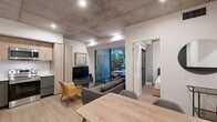 This 800 square foot apartment, located in TENTEN Downtown, showcases a harmonious blend of modern design and industrial elements. The space is characterized by its exposed concrete ceilings, which add an urban loft-like ambiance to the entire unit. Light wood flooring throughout creates a warm contrast to the industrial touches.

The open-concept layout maximizes the use of space, seamlessly connecting the living areas. The kitchen is a standout feature, boasting sleek cabinetry in a two-tone design of light wood and dark gray. High-end stainless steel appliances, including a refrigerator with water dispenser, built-in microwave, and electric range, elevate the cooking experience.

The bedroom area, while compact, is thoughtfully designed with built-in storage solutions. A custom wooden wardrobe provides ample storage space while maintaining the apartment's aesthetic continuity. The bathroom features modern fixtures, including a glass-enclosed shower, floating vanity, and LED-backlit mirror.

Large windows and glass sliding doors allow natural light to flood the space, creating a bright and airy atmosphere. An outdoor balcony or patio area, visible through these doors, extends the living space and provides a connection to the outdoors.

The apartment's furnishings are minimalist and functional, with a mix of contemporary and mid-century modern pieces that complement the overall design. Multi-functional furniture and clever storage solutions throughout make efficient use of the compact space.

This apartment exemplifies smart urban living, combining style and functionality in a well-designed package perfect for the modern city dweller.