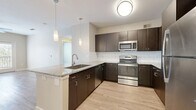This well-appointed 2-bedroom, 3-bathroom residence in Addison, TX offers a thoughtfully designed single-floor layout. The open-concept kitchen and living area serves as the heart of the home, showcasing rich dark espresso cabinetry, granite countertops, a classic white subway tile backsplash, and a full suite of stainless steel appliances including a range, microwave, dishwasher, and refrigerator. Pendant lighting and a peninsula with a double sink add both style and functionality to the kitchen space. Light wood-look flooring runs throughout, creating a clean, cohesive aesthetic. The living room is bright and airy, featuring a ceiling fan and French doors that invite natural light and provide outdoor access. The spacious primary bedroom enjoys generous natural light through large windows with outdoor views, complemented by its own ceiling fan. The en-suite primary bathroom features a granite-topped vanity with dark cabinetry, and connects to a well-organized walk-in closet outfitted with built-in shelving and hanging rods. A second bedroom offers similar bright, open characteristics. The home includes two additional closets for ample storage and a hallway connecting all areas seamlessly, making this a practical and stylish Addison residence.