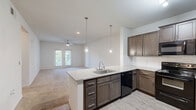 Located at 74 Sky Exchange Dr in Asheville, NC, this well-appointed single-floor, 3-bedroom, 3-bathroom home offers a thoughtfully designed open-concept layout. The kitchen is a standout feature, showcasing rich dark cabinetry, granite countertops, a subway tile backsplash, a central peninsula with pendant lighting and an undermount sink, and black appliances including a refrigerator, range, dishwasher, and microwave. Wood-look flooring in the kitchen transitions seamlessly into the living area, which is finished with plush carpeting and ceiling fans throughout. French doors in the living room open to an outdoor deck, flooding the space with natural light and providing an easy indoor-outdoor connection. The primary bedroom is generously sized, offering dual windows for natural light, a ceiling fan, and access to a walk-in closet with built-in shelving. Additional bedrooms are bright and carpeted, each with large windows. The bathrooms feature clean, white tiled tub-shower combinations with built-in shelving niches. A dedicated laundry area and multiple closets provide ample storage throughout this comfortable Asheville home.