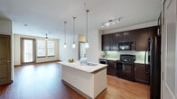 Located at 500 Coit Rd in Plano, TX, this two-bedroom, two-bathroom residence offers a thoughtfully designed single-level layout with a cohesive blend of modern finishes and functional living spaces. The open-concept kitchen and living area serves as the heart of the home, highlighted by rich dark espresso cabinetry, a green glass tile backsplash, black stainless appliances, and a granite-topped kitchen island with an undermount sink and stylish pendant lighting overhead. Warm wood-style flooring extends throughout the main living areas, complementing the bright, neutral color palette. The living room features a ceiling fan and large windows that allow abundant natural light, with access to an outdoor area via a glass door. A built-in niche adds a decorative accent along the hallway. The primary bedroom is generously sized, carpeted for comfort, and equipped with a ceiling fan and natural light. Its en-suite bathroom features a dual-sink vanity with granite countertops, dark cabinetry, tile flooring, and a full soaking tub with tiled surround. The second bedroom also features wood-style flooring and a glass door. Both closets are outfitted with multi-level shelving and hanging rods, maximizing storage throughout.