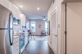 This thoughtfully designed single-floor studio offers a clean, contemporary aesthetic throughout. The open-concept layout connects the kitchen, dining, and living areas in one continuous, efficient space, creating a sense of openness despite its compact footprint.

The kitchen is well-appointed with stainless steel appliances, including a full-size refrigerator, electric range with oven, built-in microwave, and dishwasher. Crisp white cabinetry — both upper and lower — pairs with light countertops to create a bright, functional cooking space. Dark hardwood-style flooring runs throughout the unit, grounding the overall design with warmth and continuity.

Adjacent to the kitchen, a compact dining area features a round bistro-height table with bar stools, ideal for casual dining. The living area accommodates a sleeping space alongside a wall-mounted flat-screen television, with a colorful area rug and curated artwork adding personality to the warm, neutral-toned walls. A tall vertical window allows natural light to filter in, enhancing the airy ambiance.

The bathroom is clean and straightforward, finished with wood-look tile flooring, recessed lighting, and white fixtures, offering a calm, functional retreat.

Recessed lighting throughout and a ceiling fan in the living zone ensure comfort and practicality, making this a well-rounded, move-in-ready space.