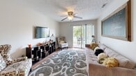 This efficiently designed single-story home in Indianapolis, IN offers three bedrooms and two bathrooms within a well-organized floor plan. The layout centers around an open-concept living, dining, and kitchen area connected by warm hardwood flooring throughout. The living room features a ceiling fan, a wall-mounted TV area with a geometric shelving unit, and a sliding glass door that opens to a private patio, bringing in natural light and outdoor views.

The kitchen is well-appointed with white cabinetry, dark granite-style countertops, black appliances including a refrigerator, electric range, and built-in microwave, and a peninsula breakfast bar with pendant lighting that seats multiple guests. Adjacent to the kitchen, the dining area is an intimate nook illuminated by a pendant light fixture.

Both bathrooms feature white vanity cabinetry with dark countertops and hardwood flooring. One bathroom includes a stacked washer and dryer unit, adding convenient in-unit laundry. The bedrooms are carpeted and each includes a window with natural light. The primary bedroom offers a closet and comfortable proportions. Textured ceilings are consistent throughout the home, contributing to its classic character.