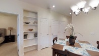 This single-floor residence offers a thoughtfully designed layout with clean, neutral interiors that create a bright and welcoming atmosphere throughout. The living area is a comfortable gathering space, featuring vaulted ceilings accented by a classic ceiling fan with integrated lighting. Soft, neutral walls provide a versatile backdrop, complemented by light-toned flooring and generous baseboard trim. The room accommodates a sectional sofa and accent seating, making it well-suited for relaxed everyday living.

Adjacent to the living area, the dining space is both functional and refined, with recessed lighting casting a warm glow over a wood dining table with coordinating chairs. A set of white panel doors lines the wall, offering access to additional rooms or storage, while a built-in open shelving unit adds a practical yet decorative element, ideal for displaying books and décor. Tile flooring runs through this area, providing durability and easy maintenance.

Throughout the space, the design emphasizes simplicity and practicality, with consistent finishes and a cohesive color palette. The overall ambiance is calm and understated, making this a versatile space that can be easily personalized to suit a variety of lifestyles.