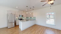 This well-appointed single-floor residence offers a thoughtfully designed open-concept layout that seamlessly connects the kitchen and living areas. The kitchen is a standout feature, showcasing light gray cabinetry, granite countertops, and a Peninsula island with pendant lighting. A soft aqua glass tile backsplash adds a distinctive pop of color, complemented by a full suite of stainless steel appliances, including a refrigerator, range, and microwave. Recessed lighting and natural light from nearby windows keep the space bright and inviting.

Light hardwood flooring flows consistently throughout the entire residence, creating a cohesive and warm aesthetic. The spacious living and dining areas each feature ceiling fans with integrated lighting and are bathed in natural light from large windows with blinds. The open floor plan, visible in the dollhouse overview, reveals multiple well-proportioned bedrooms, each with ceiling fans and windows offering exterior views.

The bathroom area features granite countertops with an undermount sink and a private water closet, reflecting the same quality finishes found throughout the home. Clean white walls, crisp white trim, and a neutral palette give the entire space a fresh, move-in-ready feel that is both modern and functional.
