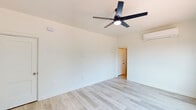 This well-appointed single-floor unit offers a clean, modern aesthetic throughout, highlighted by light-toned hardwood flooring that runs seamlessly across all living areas. The open living space is bright and airy, featuring large windows that frame outdoor views of lush greenery and the surrounding neighborhood, allowing natural light to fill the room. A sleek ceiling fan with built-in lighting adds both function and style, complemented by a wall-mounted mini-split system for efficient climate control.

The kitchen is thoughtfully designed with crisp white shaker cabinetry, granite countertops with warm, natural veining, a stainless steel undermount sink positioned beneath a window overlooking greenery, and a professional-grade stainless steel gas range paired with an overhead ventilation hood. A stainless steel refrigerator completes the suite of appliances.

The bathroom is a standout space, featuring bold black-and-white patterned encaustic floor tiles that contrast beautifully with the marble-look wall tile in the shower enclosure. A vintage-inspired pendant light and a compact vanity add character to the refined, monochromatic palette.

The bedroom is generously proportioned with vaulted ceilings, soft white walls, and its own ceiling fan and mini-split unit, creating a comfortable and tranquil retreat. Throughout, the space maintains a cohesive, contemporary design with clean lines and a neutral color palette.
