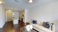 This well-designed single-floor residence offers a seamless open-concept layout that connects the living and kitchen areas, creating a cohesive and functional living environment. The living area is bright and inviting, featuring rich dark hardwood flooring that flows throughout the space and crisp white walls that enhance the sense of openness. A ceiling fan with a flush-mounted light fixture provides both comfort and illumination. The kitchen is thoughtfully designed with cream-toned cabinetry, stainless steel appliances including a refrigerator, microwave, and range, and a peninsula with pendant lighting overhead, offering both prep space and a casual dining option. A sleek sink with modern fixtures completes the kitchen. Track lighting in the kitchen ensures excellent task lighting throughout. The clean, neutral color palette runs consistently across both spaces, lending a polished and cohesive aesthetic. The combination of warm wood flooring, white walls, and stainless steel accents gives this residence a contemporary yet welcoming ambiance, well-suited for both everyday living and entertaining.