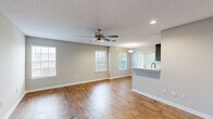 This single-story, 1-bedroom, 1-bathroom residence offers a thoughtfully designed layout that maximizes functionality and comfort. The open-concept living room serves as the heart of the home, featuring rich hardwood flooring, a textured ceiling, recessed lighting, and a ceiling fan. Multiple windows dressed with white blinds fill the space with natural light, while a kitchen pass-through with a built-in sink connects seamlessly to the living area. The kitchen is well-equipped with dark wood cabinetry, white quartz countertops, a tile backsplash, and stainless steel appliances, including a range, microwave, refrigerator, and double-basin sink. The spacious bedroom is finished with plush carpeting and a ceiling fan, and it connects to a generous walk-in closet outfitted with dual wire shelving systems. The bathroom features hardwood-style flooring, a tub/shower combination, and a dark wood vanity consistent with the kitchen's design aesthetic. The dedicated laundry area includes an in-unit washer and wire shelving for additional storage. Neutral gray tones throughout the home create a clean, cohesive aesthetic well-suited for a variety of living styles.