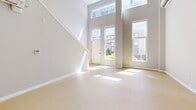 Located at 121 N 2nd St in Philadelphia's historic Old City neighborhood, this two-story unit spans 930 square feet across a spacious main floor (610 sq ft) and an upper loft level (320 sq ft). The main floor is immediately striking thanks to its dramatic double-height ceilings and floor-to-ceiling windows flanking the entry door, flooding the open living area with abundant natural light and offering views of the surrounding streetscape. Light-toned hardwood-style flooring runs throughout, reinforcing the unit's clean, modern aesthetic. The contemporary kitchen features two-tone cabinetry — white upper cabinets paired with slate-gray lower cabinets — white quartz countertops, a subway tile backsplash, and a full suite of stainless steel appliances including a refrigerator, electric range, over-the-range microwave, and dishwasher. The full bathroom is finished with large-format dark tile flooring, a glass-enclosed walk-in shower with grab bars, a toilet, and a gray vanity with a white countertop. A hallway connects the main living areas and provides access to the staircase leading to the upper loft level, which features warm hardwood-style flooring, a tray ceiling detail, and an open railing overlooking the main floor below.